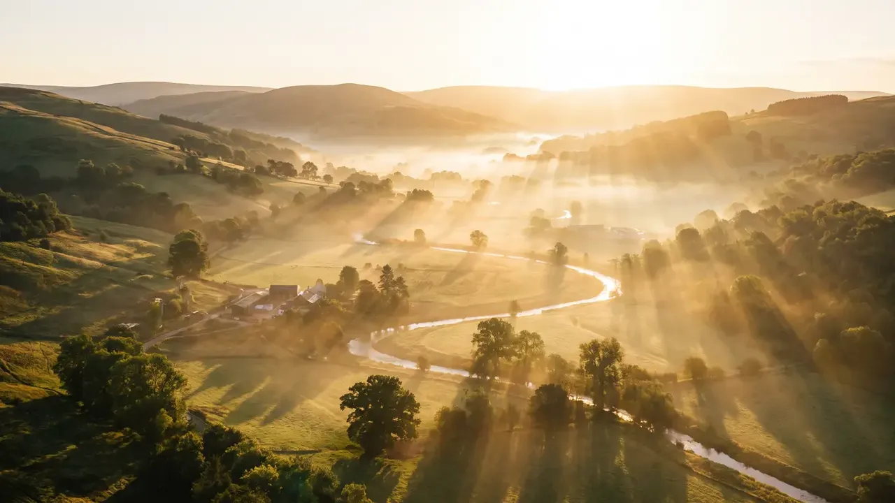 The sun rising over rolling hills, the valley filling with morning light